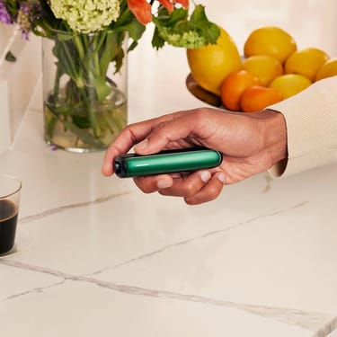 Ruka koja drži Ploom AURA uređaj sa prednjom maskom u Amazon Green boji

