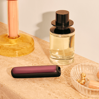 Ploom AURA uređaj sa Dark Orchid prednjom maskom na komodi
