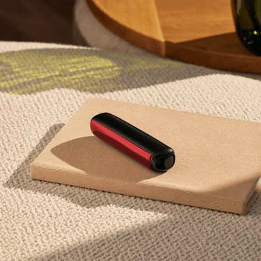 Ploom AURA uređaj sa Lava Red prednjom maskom na stolu
