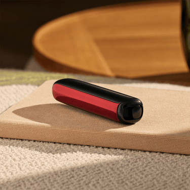 Ploom AURA uređaj sa Lava Red prednjom maskom na stolu
