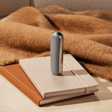 Ploom AURA uređaj sa Lunar Silver zadnjom maskom na sveskama
