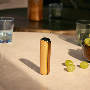 Ploom AURA uređaj sa Mango Sorbet zadnjom maskom na stolu
