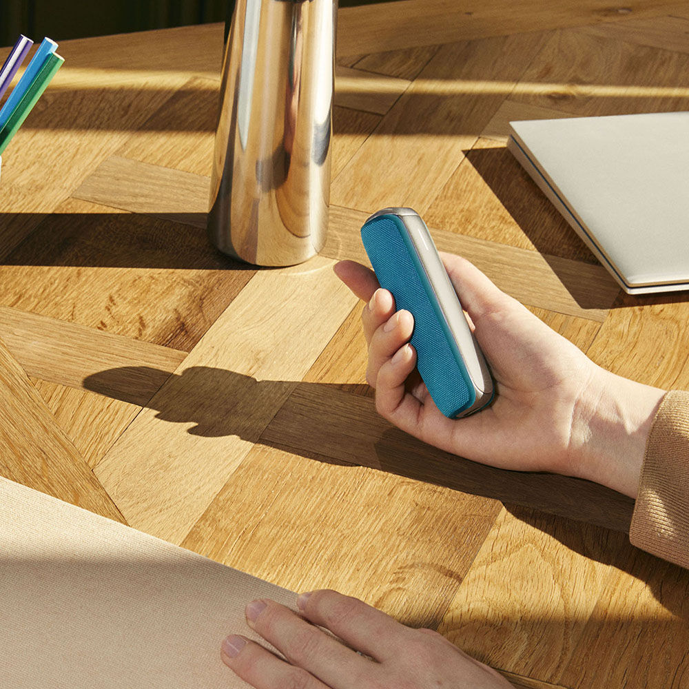 Ruka koja drži Ploom AURA uređaj sa Ocean Blue zadnjom maskom
