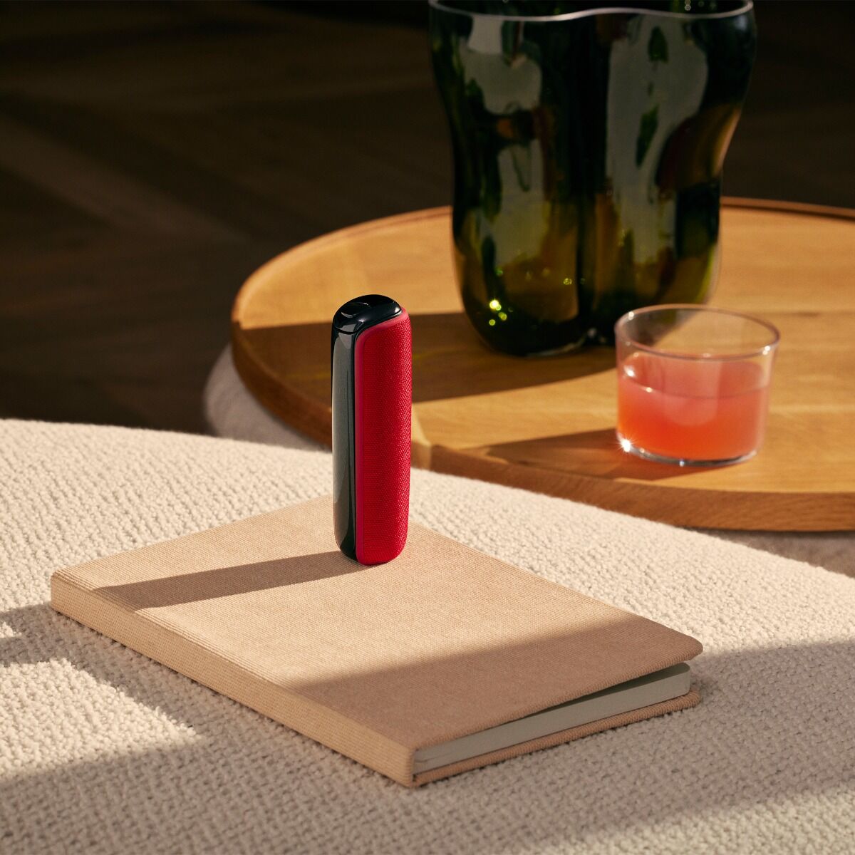 Ploom AURA with Lava Red back cover placed on top of a book on a table
