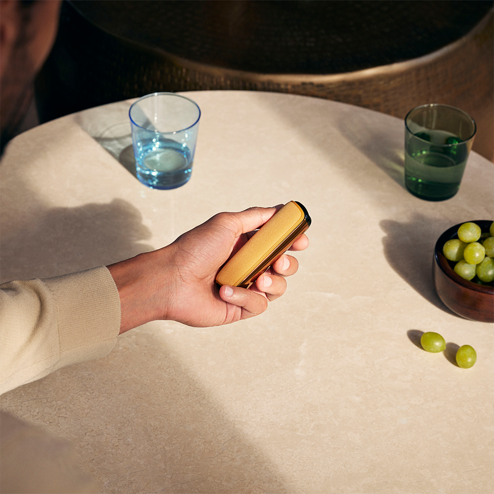 Ruka koja drži Ploom AURA uređaj sa zadnjom maskom u Mango Sorbet boji
